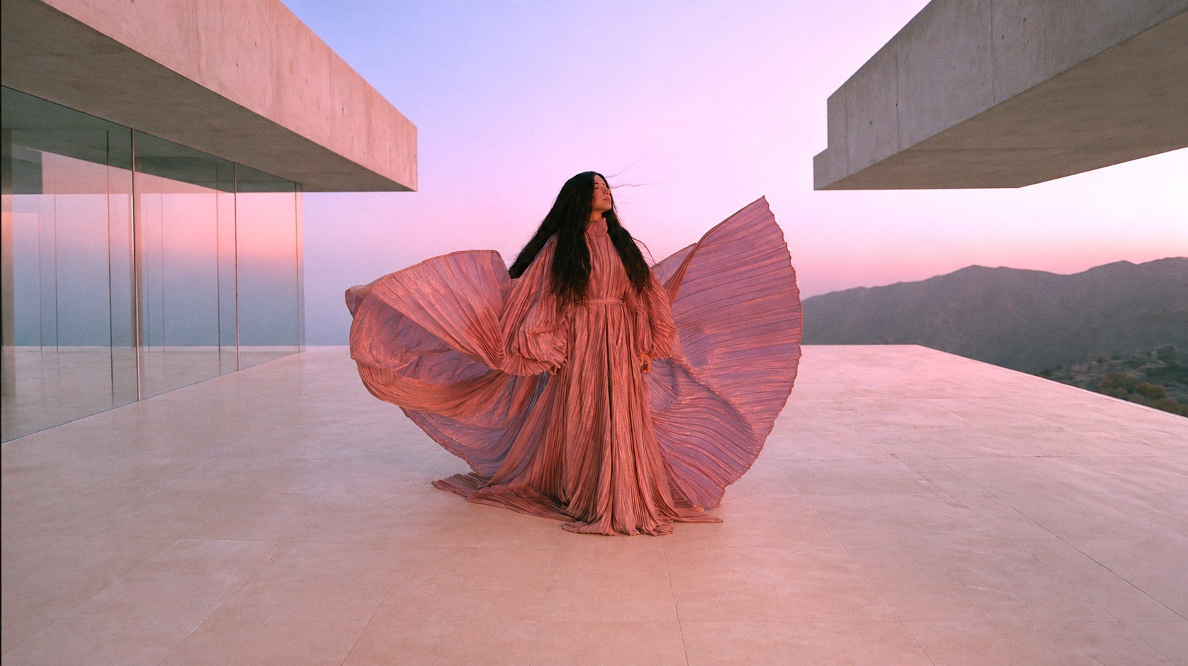 Mulher com um vestido rosado esvoaçante no terraço de concreto, ao amanhecer